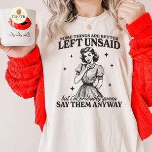 May include: White t-shirt with black text that reads "Some things are better left unsaid, but I'm probably gonna say them anyway". A black and white illustration of a woman with her finger to her lips is above the text.