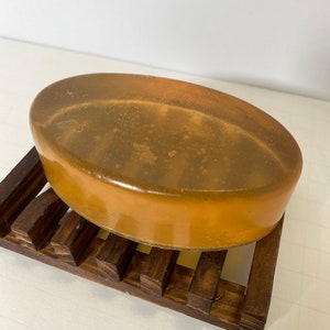 May include: A translucent amber-colored soap bar with flecks of gold shimmer, resting on a wooden soap dish.