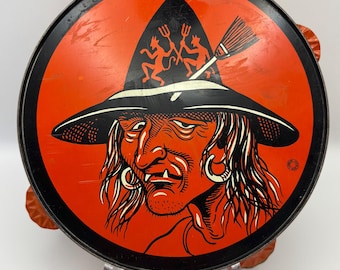 May include: Vintage Halloween serving tray with a witch illustration. The tray features a black rim, an orange background, and a witch wearing a black hat with a broom and devil figures. The tray is round and has decorative edges.