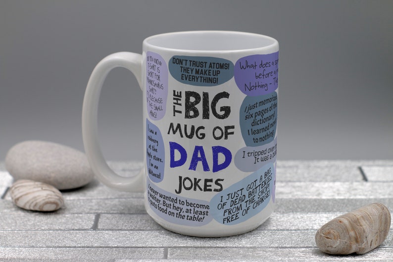 May include: White ceramic mug with the text "The Big Mug of Dad Jokes" in black and blue. The mug is covered in speech bubbles with various jokes. The mug has a large handle.