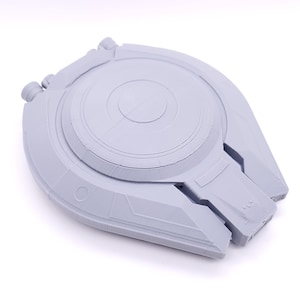 Puede incluir: Un modelo de nave espacial impreso en 3D de color gris con una parte superior circular y una parte inferior puntiaguda.