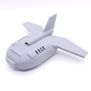 May include: A gray 3D printed model of a futuristic spaceship with a rounded body and wings. The spaceship has a small engine on the back and a series of air vents on the side.
