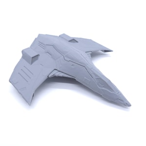 May include: A grey model of a futuristic aircraft or spacecraft. The model has a sleek, angular design with detailed paneling and a pointed nose. The wings are swept back, and the overall shape suggests speed and advanced technology.