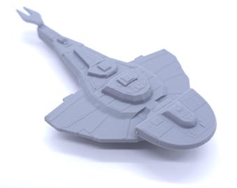 Puede incluir: Modelo gris claro de una nave espacial con un diseño distintivo. La nave espacial presenta una larga cola puntiaguda y un cuerpo ancho y plano con detalles de superficie. El modelo está sobre un fondo blanco.