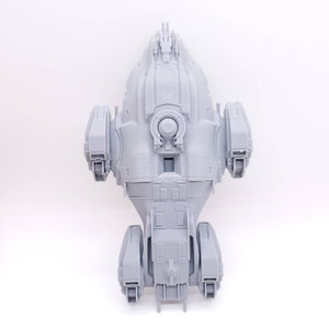 May include: A gray 3D printed model of a spaceship with a rounded body and a long, thin tail. The spaceship has a large, round window in the front and several smaller windows on the sides.