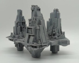 May include: A 3D printed model of a futuristic city with three towers connected by a platform. The towers are made of gray plastic and have a variety of geometric shapes.