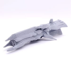 May include: A gray 3D printed model of a spaceship with a long, slender body and a pointed nose. The spaceship has a detailed design with multiple fins and a series of engines at the rear.