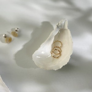 May include: Three gold rings stacked inside a white seashell. The seashell is on a white surface.