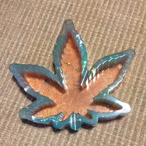May include: A teal blue resin leaf shaped ashtray with a glittery finish. The inside of the ashtray is a light brown color.