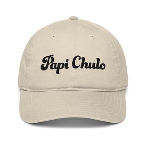 May include: A beige baseball cap with black embroidered text that reads "Papi Chulo" in a retro font.