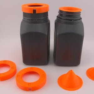Puede incluir: Dos botellas de plástico gris oscuro con tapas naranjas y varios accesorios naranjas. Los accesorios incluyen dos piezas circulares con las letras "B" y "C" y dos piezas en forma de cono. Las botellas son rectangulares con esquinas redondeadas.