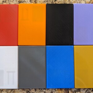 May include: Eight square tiles in different colors: red, orange, black, purple, white, gray, blue, and yellow.