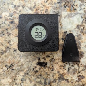 May include: A black digital hygrometer and thermometer with a display showing 79.0 degrees Fahrenheit and 28 percent humidity. The device is mounted on a wall with a black plastic bracket.