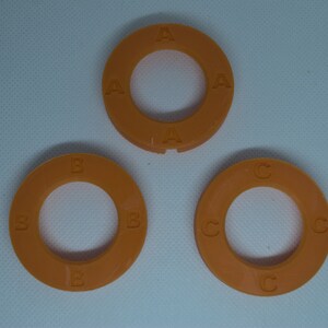 May include: Three orange plastic rings with letters A, B, and C printed on them. The rings are different sizes.
