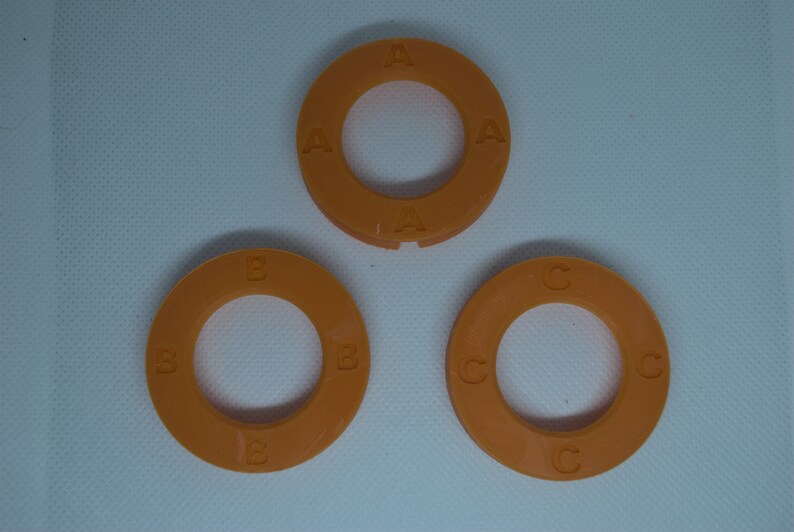 May include: Three orange plastic rings with letters A, B, and C printed on them. The rings are different sizes.