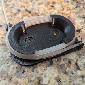 May include: A black 3D printed filament holder with a clear filament spool inside.