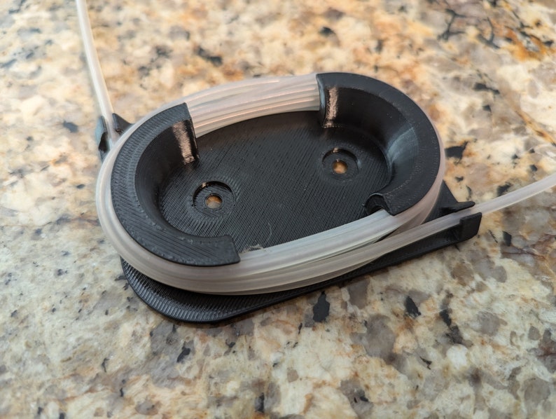 May include: A black 3D printed filament holder with a clear filament spool inside.