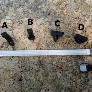 May include: Four black plastic brackets labeled A, B, C, and D, with a ruler and a small gray device with a black cord.