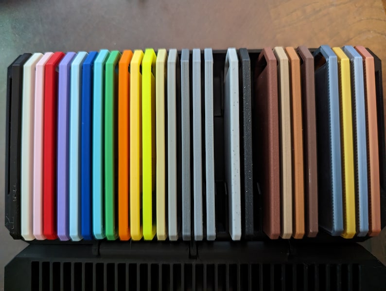 May include: A set of 25 colorful silicone phone cases in a variety of colors, including pink, red, blue, green, yellow, orange, gray, brown, and black. The cases are arranged in a row and are all the same size.