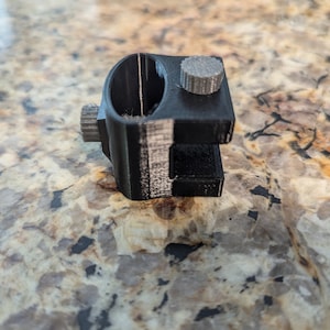 May include: A black 3D printed camera mount with a gray knob. The mount has a circular opening and a slot for attaching a camera.