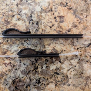 May include: Two black plastic cable organizers with white cords attached. The organizers have a curved shape and are designed to hold cables in place.