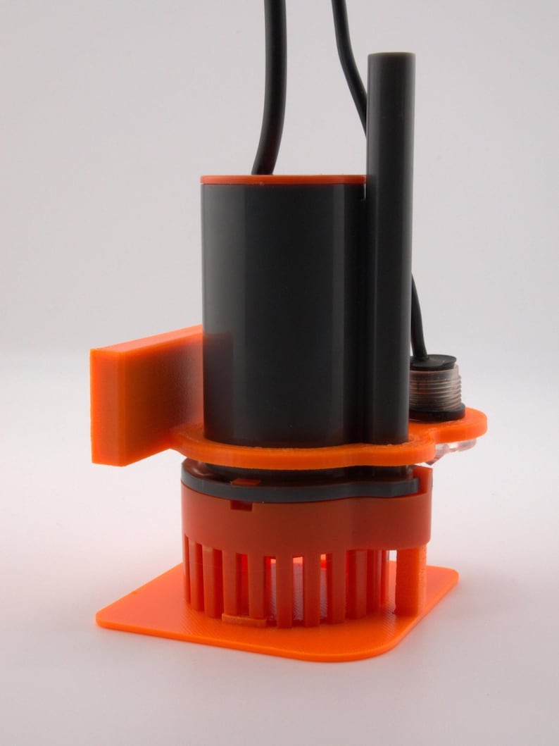 May include: An orange and black submersible pump with a square base and a cylindrical body. The pump has a series of vertical orange fins at the bottom and a black cable extending from the top. The design includes an orange bracket on the side.