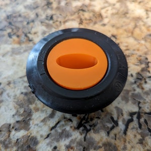 May include: Black plastic knob with an orange center and a small oval opening. The knob has numbers printed around the edge.