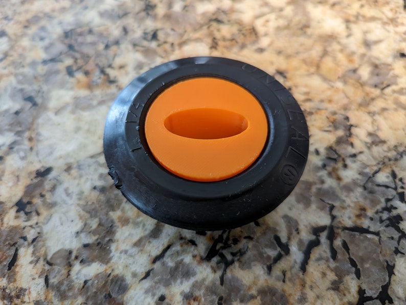 May include: Black plastic knob with an orange center and a small oval opening. The knob has numbers printed around the edge.
