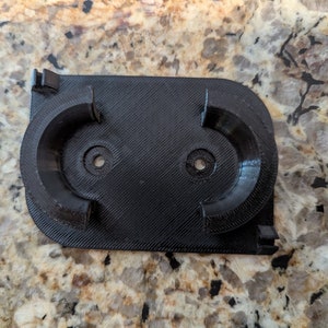 May include: A black 3D printed wall mount with two circular cutouts for holding items.