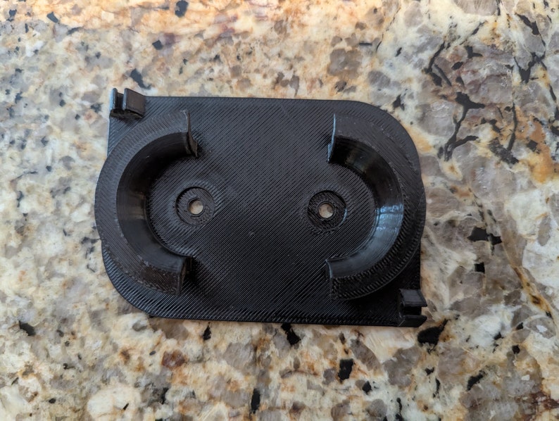 May include: A black 3D printed wall mount with two circular cutouts for holding items.