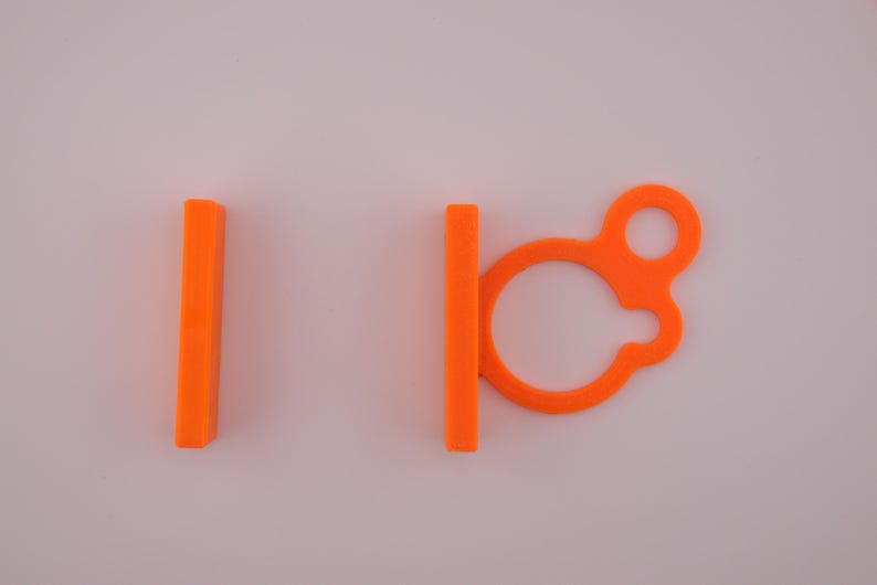 May include: Bright orange plastic cable organizers. One is a solid rectangle, and the other has a loop and a clasp. These are designed to keep cables tidy and organized. The items are set against a plain white background.