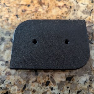 May include: Black plastic rectangular plate with two holes. The plate has a slightly rounded edge.
