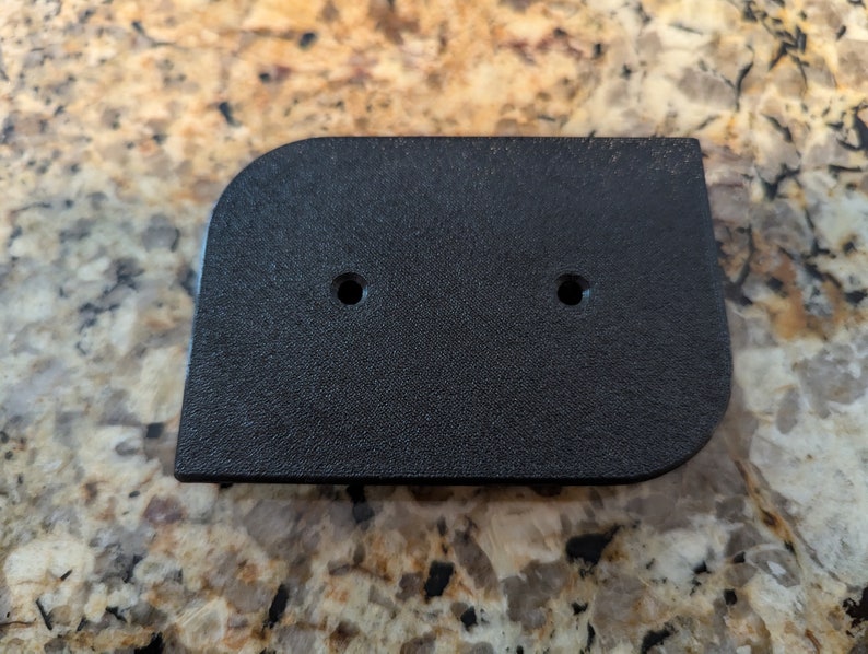May include: Black plastic rectangular plate with two holes. The plate has a slightly rounded edge.
