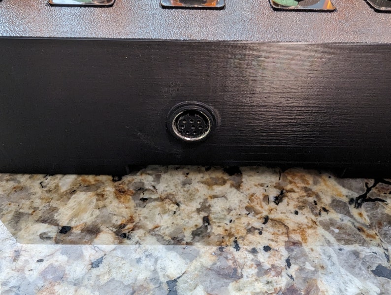 Puede incluir: Primer plano de un dispositivo electr&oacute;nico negro con un conector redondo plateado en la parte inferior.