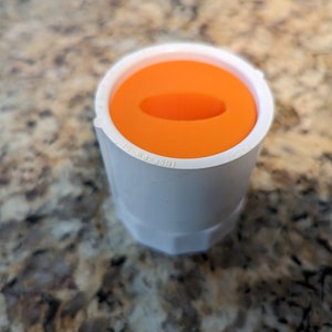 May include: A white plastic pipe fitting with an orange cap. The cap has a small hole in the center.
