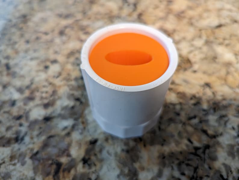 May include: A white plastic pipe fitting with an orange cap. The cap has a small hole in the center.