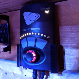 May include: Black electronic device labelled "MP40 W" with a fish logo and the words "QUIET DRIVE." It features buttons, a central dial with a red glow, and small lights. The device is mounted on a wooden surface.