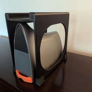 May include: A black metal stand with a shelf for storing a silver iron with an orange handle. The stand is on a dark brown wooden surface.