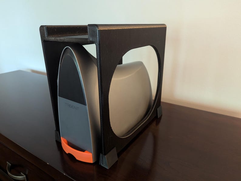May include: A black metal stand with a shelf for storing a silver iron with an orange handle. The stand is on a dark brown wooden surface.