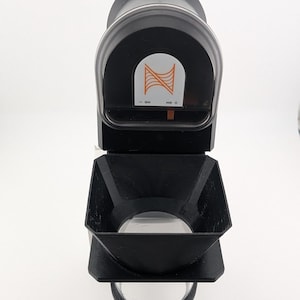 May include: A black and clear device with a clear lens and a black handle. The device has an orange and white logo on the top. The device is on a white background.