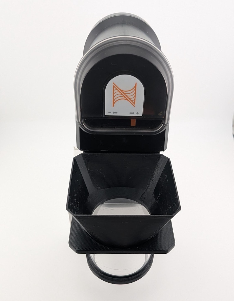 May include: A black and clear device with a clear lens and a black handle. The device has an orange and white logo on the top. The device is on a white background.