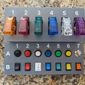 May include: A gray panel with two rows of switches and buttons. The top row has six toggle switches labeled 1 through 6. The bottom row has seven buttons labeled 1 through 7, and two rows of toggle switches labeled A and B.