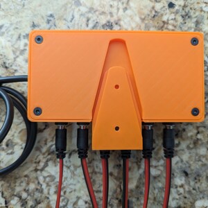 May include: Orange plastic enclosure with four black connectors and a wall mount. The enclosure has two black screws on each side.