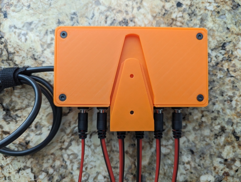May include: Orange plastic enclosure with four black connectors and a wall mount. The enclosure has two black screws on each side.