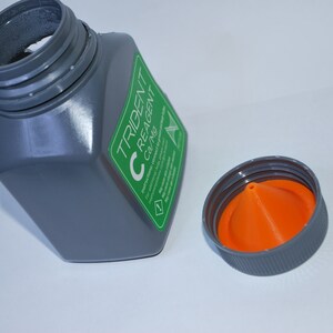 Pu&ograve; includere: Una bottiglia di plastica grigia con un'etichetta verde che dice "TRIDENT C REAGENT C37MG". La bottiglia ha un tappo grigio con un beccuccio a forma di cono arancione.