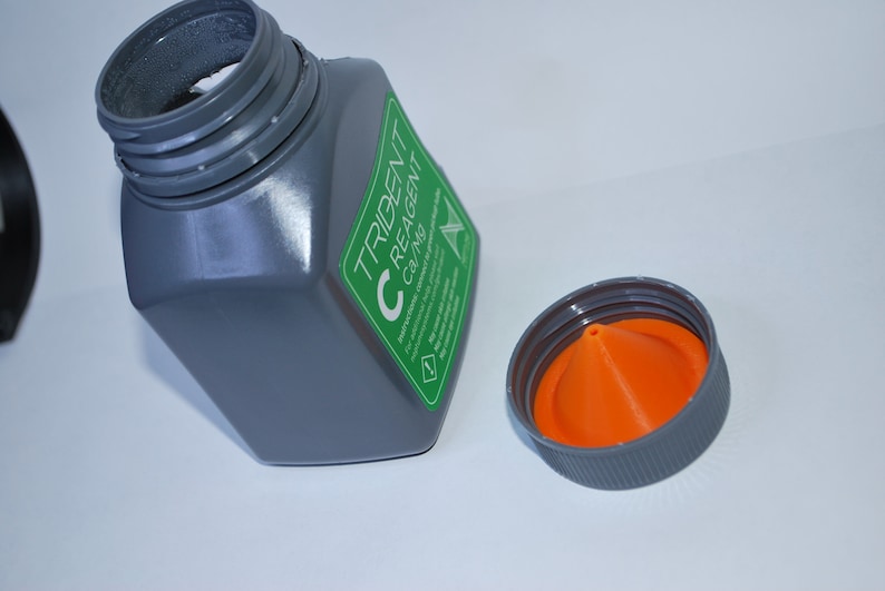 Pu&ograve; includere: Una bottiglia di plastica grigia con un'etichetta verde che dice "TRIDENT C REAGENT C37MG". La bottiglia ha un tappo grigio con un beccuccio a forma di cono arancione.