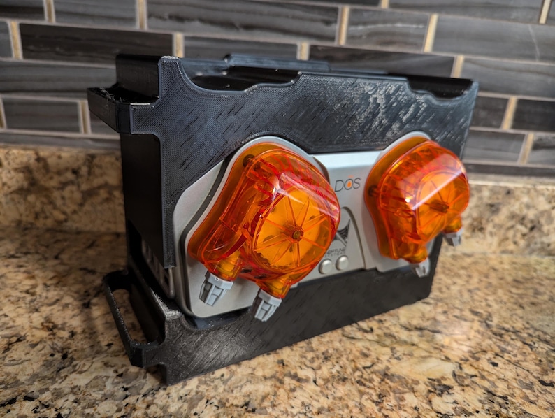 May include: A black plastic box with two orange and silver pumps labeled "DOS" mounted on the front.