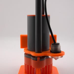 May include: An orange and gray submersible pump with a black cable and a clear, diamond-shaped component. The pump has a cylindrical body and a square base. The design includes vertical orange fins.
