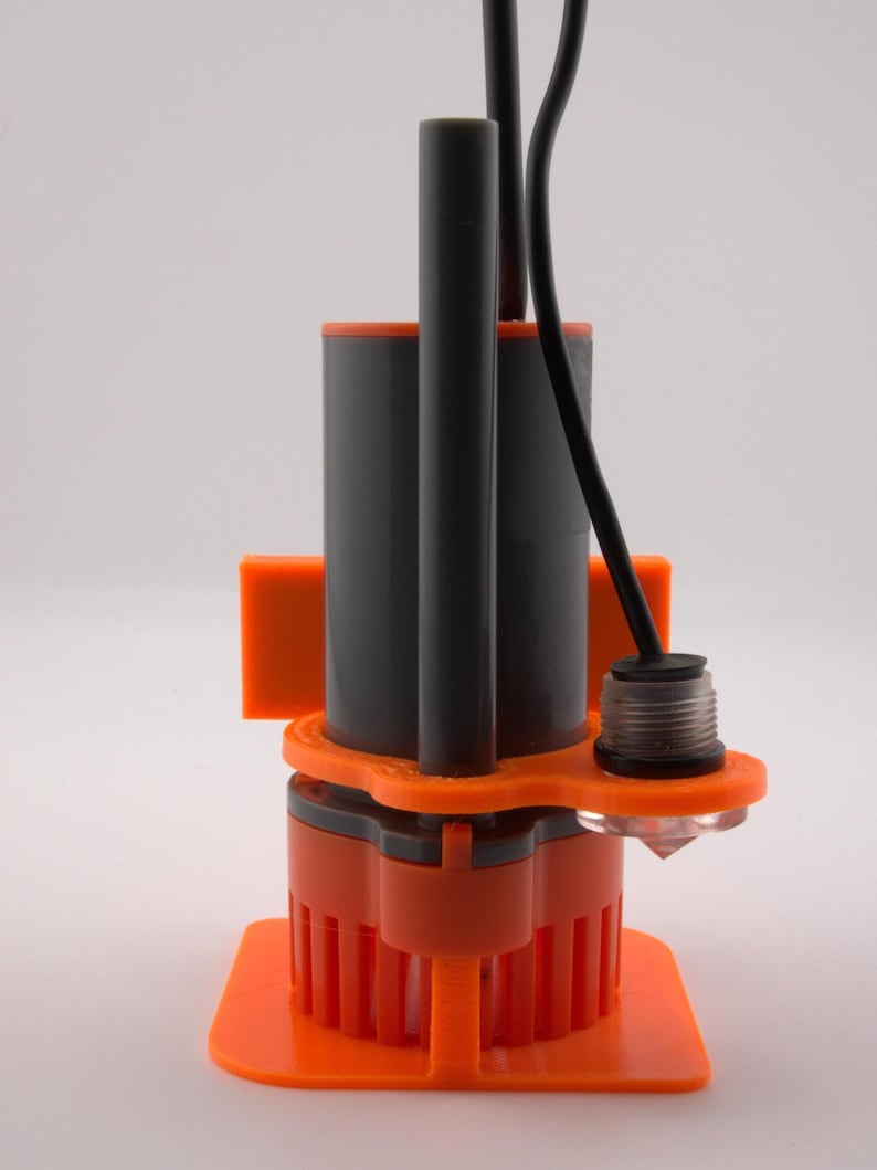May include: An orange and gray submersible pump with a black cable and a clear, diamond-shaped component. The pump has a cylindrical body and a square base. The design includes vertical orange fins.