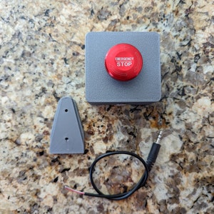 May include: A grey plastic box with a red emergency stop button. The box has a small grey plastic bracket and a black wire with a 3.5mm audio jack.